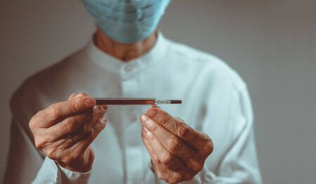 Coronavirus quarantine and Air pollution pm2.5 concept. Old sick woman wearing respirator mask for protect holds thermometer.の写真素材