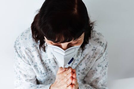 Coronavirus quarantine Covid-19 concept. Face of old sick woman wearing respirator mask for protect praying with folded hands.の写真素材