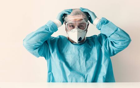 Coronavirus Covid-19 concept. Tired elderly doctor in glasses and a respirator mask for protection...
