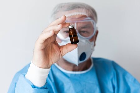 Coronavirus Covid-19 concept. Doctor in glasses and a respirator mask for protection holds a vaccine...