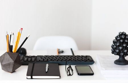 Home office, modern workplace: white table, keyboard laptop computer, concrete holder with pencils...