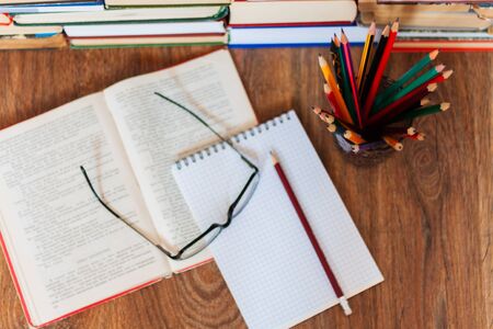Open textbook, notebook, glasses, pencils in holder, stack of old book on wooden table, education concept background, many books piles with copy space for textの写真素材