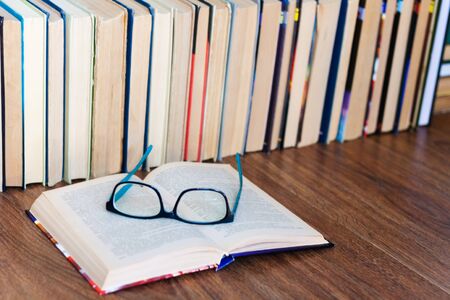Open textbook, glasses, stack of old book on wooden table, education concept background, many books...
