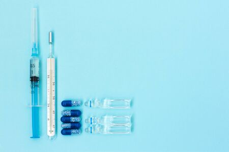 Thermometer, pills, injection ampoules, syringe for vaccination on a blue background, healthcare...
