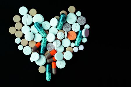 Heap of colorful pills in the shape of a heart, tablets and capsules on black background. Drug prescription for treatment medication health care concept, top view with copy spaceの写真素材