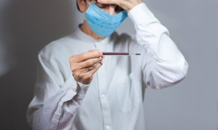 Coronavirus quarantine and Air pollution pm2.5 concept. Old sick woman wearing respirator mask for protect holds thermometer.の写真素材