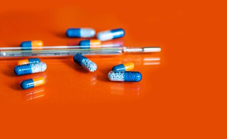 Thermometer and heap of pills, tablets, capsules on orange background. Drug prescription for...