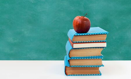 Back to school, pile of books and red apple with empty green school board background. Distance home education. Quarantine concept of stay homeの写真素材
