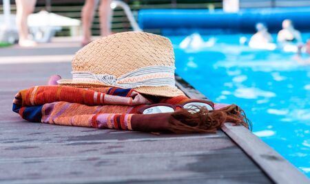 Vintage summer wicker straw beach hat, sun glasses, cover-up beachwear wrap near swimming pool, tropical backgroundの写真素材