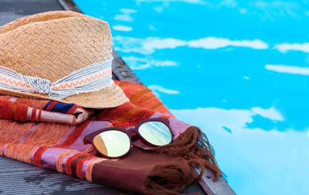 Vintage summer wicker straw beach hat, sun glasses, cover-up beachwear wrap near swimming pool, tropical backgroundの写真素材