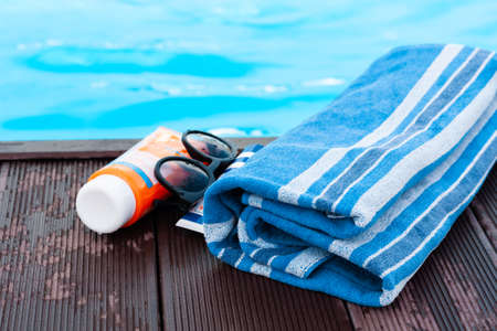 sun glasses, tube of sunscreen cream, blue towel near swimming pool, tropical backgroundの写真素材