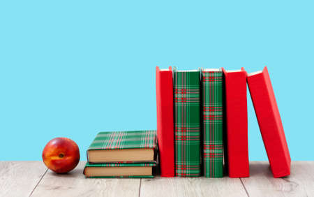 Back to school, pile of books in colorful covers and red peach on wooden table with blue background. Distance home education. Quarantine concept of stay homeの写真素材