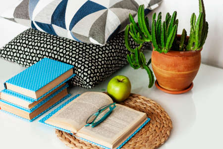 Cozy home interior decor: cup of coffee, stack of books, plants in pots, open book and green apple...