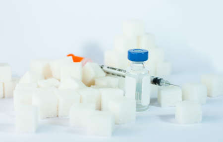 Sugar addiction, insulin resistance, unhealthy diet, sugar cubes pyramid, bottles of insulin and syringe for vaccinationon white background, diabetes protection medical concept, top viewの写真素材