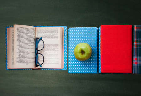 Open textbook, pile of books in colorful covers and apple with blackboard background. Distance home education. Back to school, quarantine concept of stay homeの写真素材