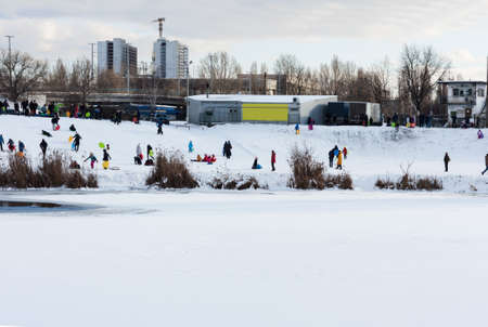 Children and their parents sledding from a snow slide in a city park with a frozen lake in Kiev, Ukraineのeditorial素材