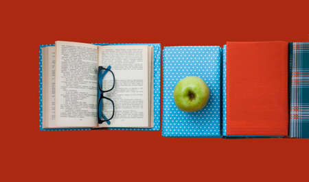 Open textbook, pile of books in colorful covers and apple on red pink orange background. Back to school distance home education.の写真素材