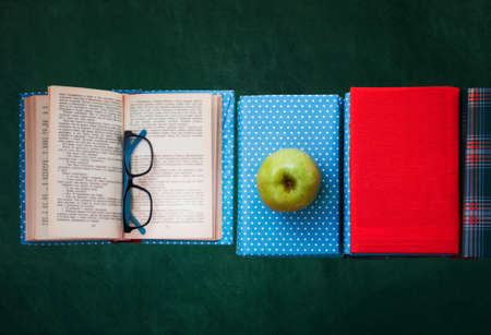 Open textbook, pile of books in colorful covers and apple with blackboard background. Distance home education. Back to school, quarantine concept of stay homeの写真素材