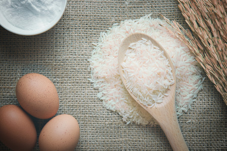 Rice in ladle with eggs and flour ingredient on burlap material background. top view. vintage color....