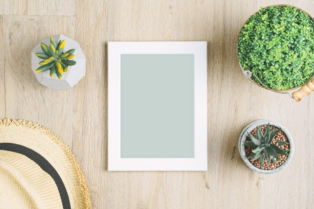 Blank photo frame placed on a wooden floor adorned with potted plants and hats.の写真素材