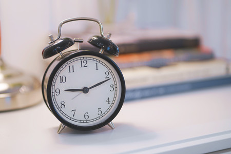 Black alarm clock and book on white table background.の写真素材