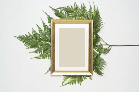 Stylish minimal composition with photo frame and green leaves on a white wooden background. Empty photo frame and green leaves. flat lay, top view.の写真素材