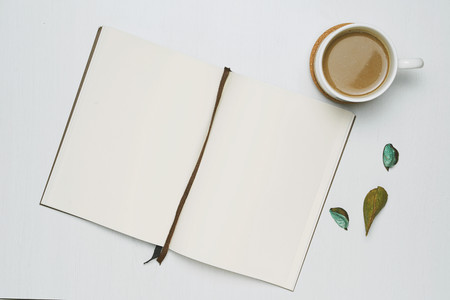 Coffee cup with open notebook on white wooden background. Minimal flat lay, Top view.