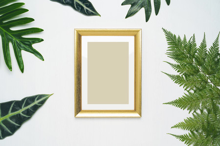 Stylish minimal composition with photo frame and green leaves on a white wooden background. Empty photo frame and green leaves. flat lay, top view.の写真素材
