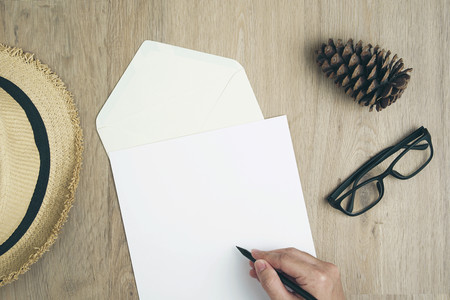 Close up hand man writing by pencil on blank paper letter on wood table with envelope, pinecone, hats and glasses.の写真素材