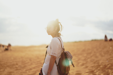 Young female exploring the desert, sandy beach with bag and camera.