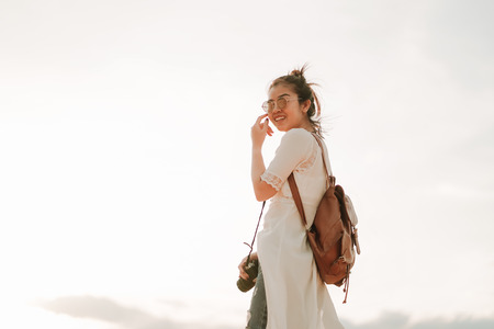 Young female exploring the desert, sandy beach with bag and camera.