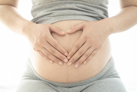 Close up of pregnant woman making heart shape hand sign on her bare tummy.