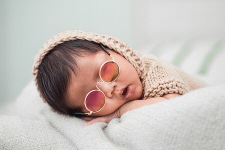 Adorable newborn baby peacefully sleeping on a white blanket. He is wearing sunglasses.の写真素材