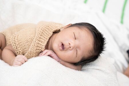 Happy cute adorable Asian baby boy with black hair lying a white blanket.