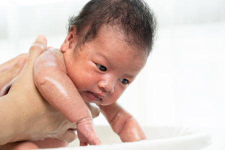 Newborn is being bathed by her mother using tub at home.の写真素材