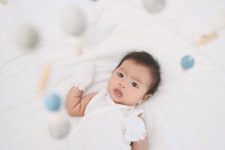 Cute baby girl is watching baby crib mobile at home. Baby crib mobile. Toys above the baby crib. Hanging soft balls for the child.の写真素材