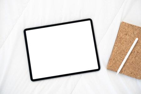 Top view of tablet with a white screen lies on a bed with notebook and digital pen.の写真素材