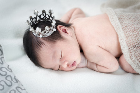 Newborn baby girl sleeping and wearing a silver crown.の写真素材