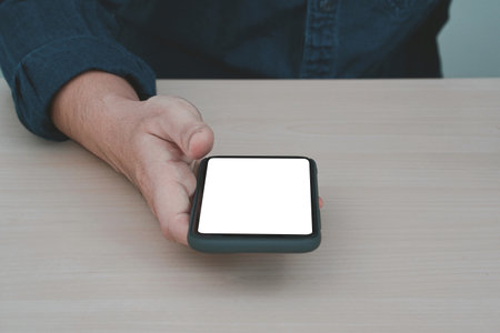Mockup image blank screen smartphone. Blank white smartphone held by male hand on wooden background.の写真素材