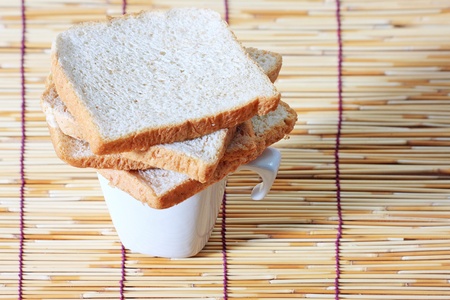 bread over the cup on bamboo plate,many slice of bread from whole wheat flour and white cup on...