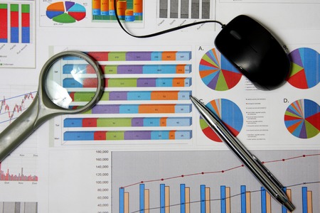 Business finance chart with magnifying glass, silver pen and mouse on table.の写真素材