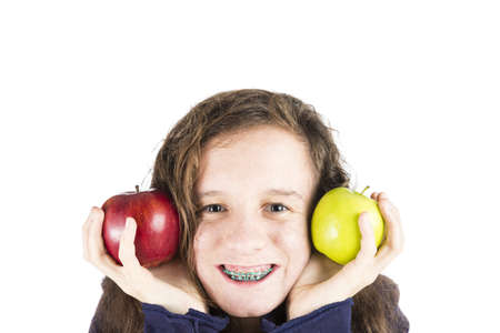 A teenage girl holding a red and a green apple close to her faceの写真素材