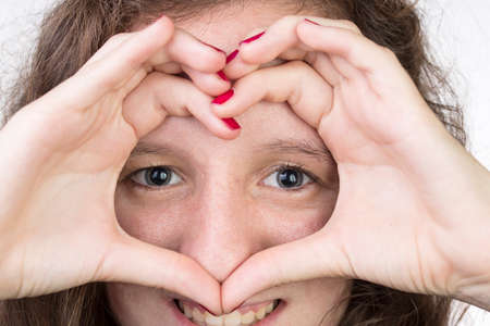 Teen with her hands held in a heart shape over her face の写真素材