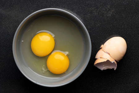 A closeup of eggs beaten in a bowl next to the eggshell on a black table