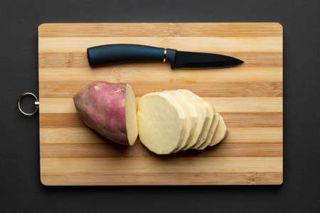 A closeup of a sliced purple sweet potato on a wooden board with a knife