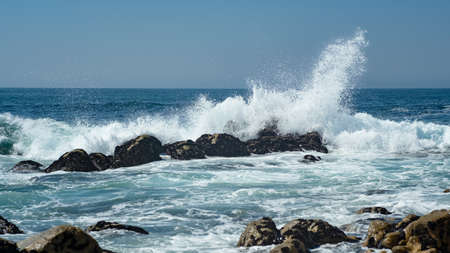 Wave splashing against rocks in the ocean, sending spray into the air. Bright sunny day in summer.の写真素材