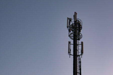 Cell phone tower communications antenna or mast in silhouette at dusk against dark blue sky. Copy...