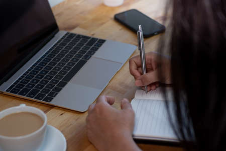 Woman working from home with laptop, notepad, and smartphone.