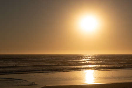 Sun reflected on ocean and wet sand at sunset on the beachの写真素材