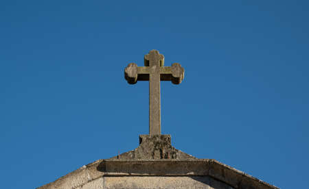 Old stone cross atop Catholic chapel in rural Portugal against blue sky.の写真素材
